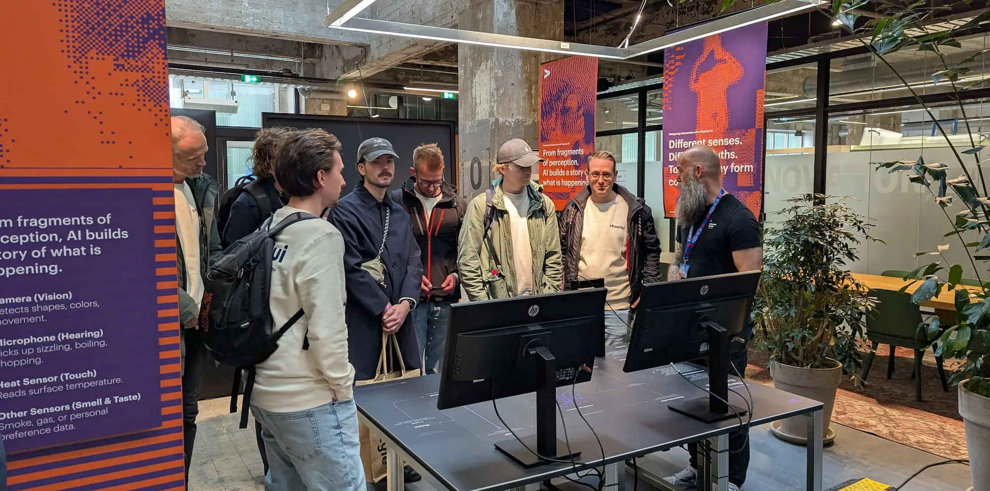 Collega’s van Stuurlui tijdens de Dutch Design Week luisteren naar een presentatie over ‘Designing Interaction with Physical AI’, omringd door kleurrijke banners en interactieve schermen in een industriële setting.